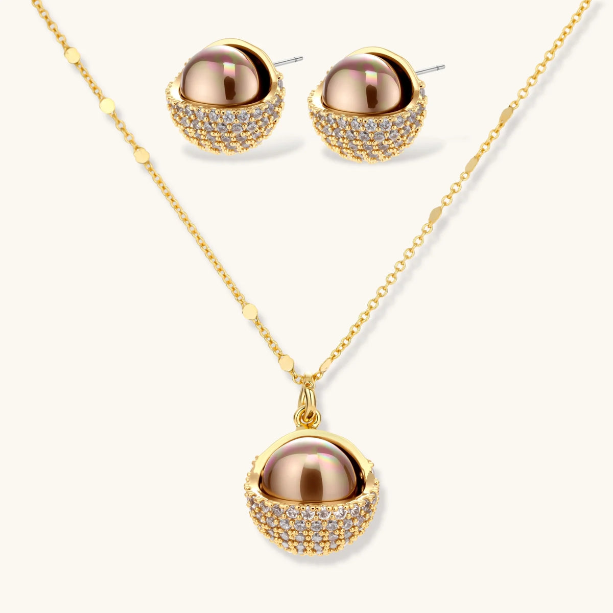 Elegant spherical pendant necklace and earrings set featuring crystal-pavé bottom half in gold or silver finish on white background.
