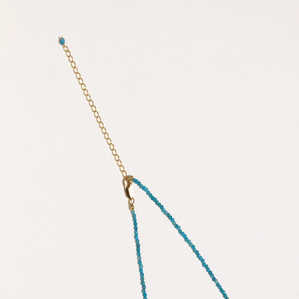 Delicate gold vermeil necklace with teal apatite beads and freshwater pearl on white background.