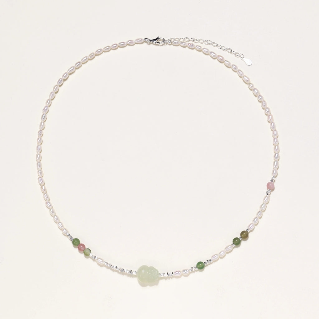 Delicate pearl necklace with pale green serpentine jade centerpiece and colorful agate beads on cream background