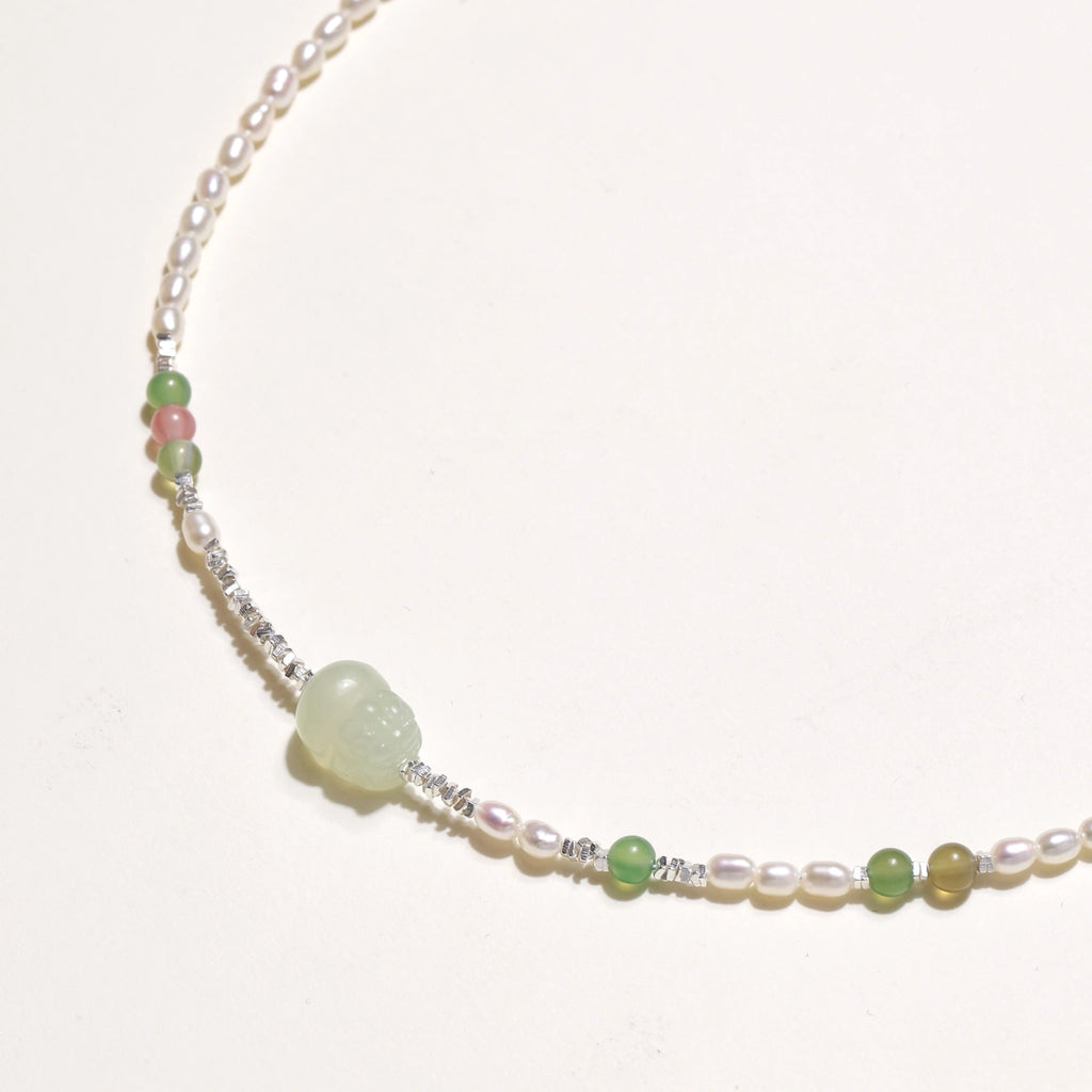 Delicate pearl necklace with pale green serpentine jade centerpiece and colorful agate beads on cream background
