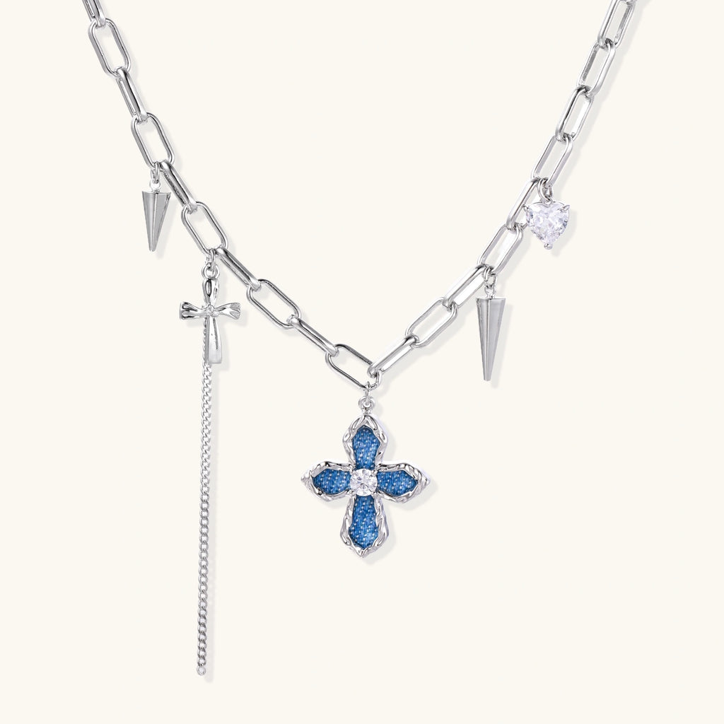 White gold plated chain necklace with blue textured cross pendant, spike charms, and mini cross detail on beige background