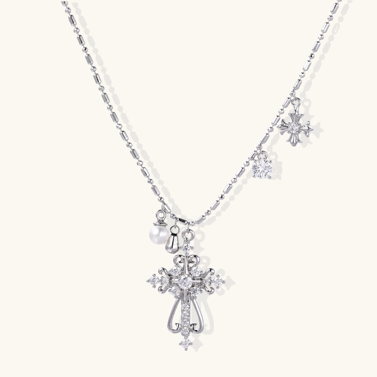 Ornate white gold-plated cross pendant with zirconia stones and pearl accents on adjustable silver chain against cream background