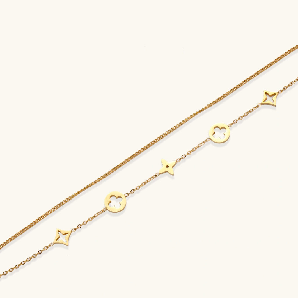 Double-layer gold-plated bracelet with quatrefoil and star charms on cream background, 18K gold finish.