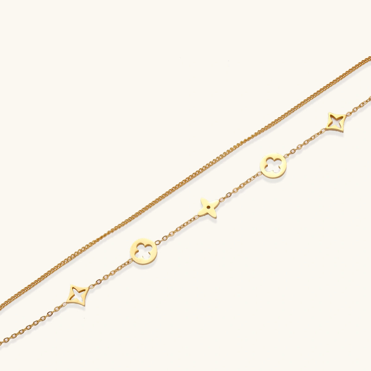 Double-layer gold-plated bracelet with quatrefoil and star charms on cream background, 18K gold finish.
